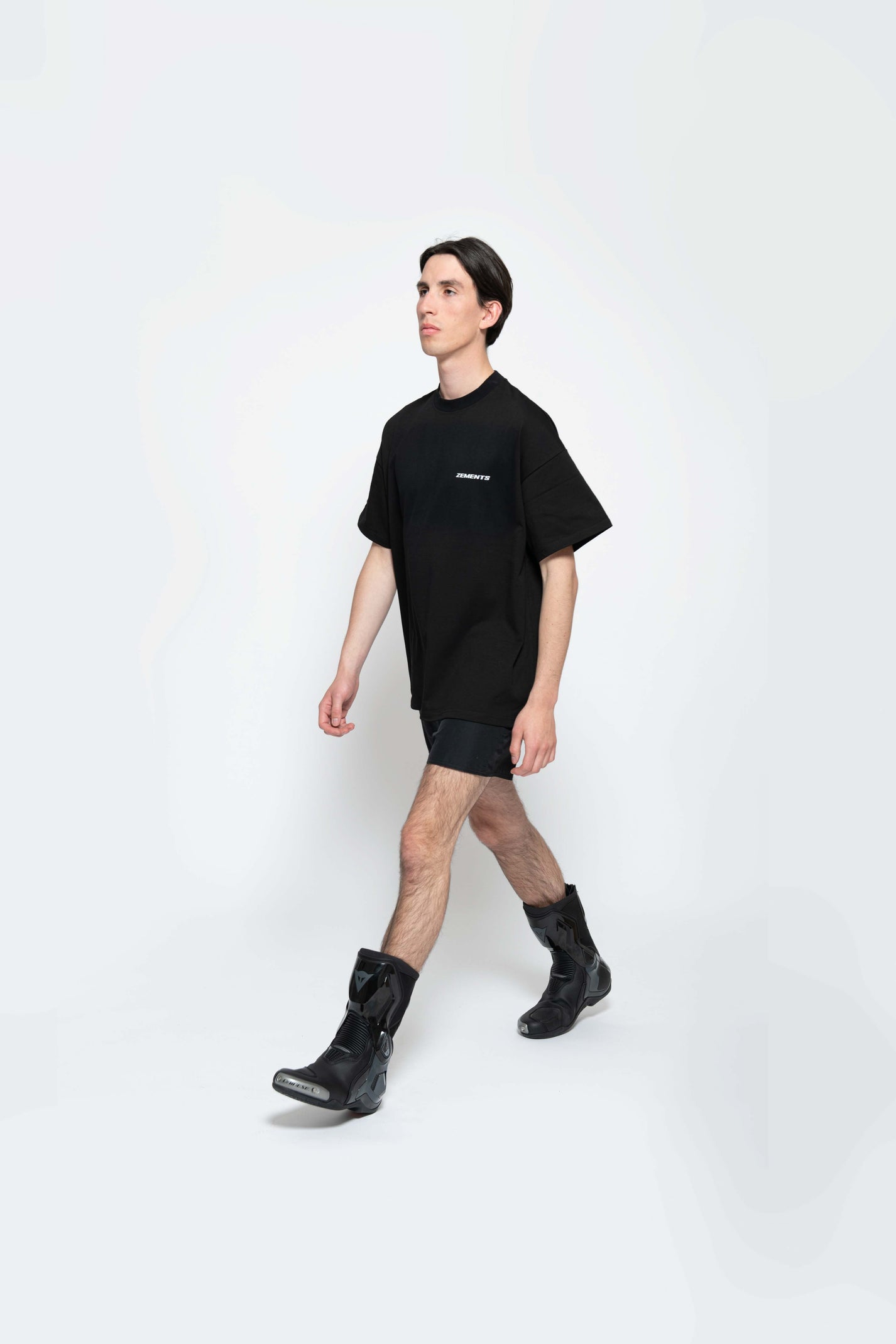 Auf weißem Hintergrund läuft männliches Model nach links vorne. Das Model hat das schwarze Sweet Pain Issue T-shirt an. Dazu schwarze Biker-Stiefel. 